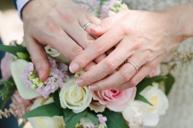 İki el, neşeli bir açık hava seremonisi sırasında canlı bir çiçek buketi tutarken alyansları sergiler..