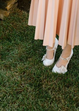 Beyaz çiçekli ayakkabılar açık hava etkinliğinde canlı yeşil çimenler üzerinde yumuşak pembe bir elbiseyle eşleşiyor..