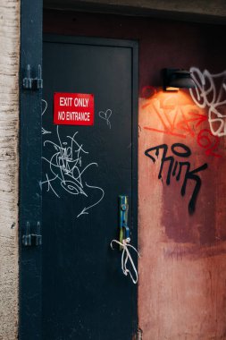 Giriş tabelası olmayan karanlık bir kapı bir ara sokakta duvar yazısının yanında durur, akşam ışığı ile aydınlatılır..