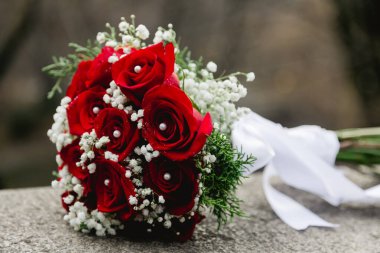 Göz kamaştırıcı bir buket, açık havada kayaların üzerinde duran narin beyaz çiçeklerle tamamlanmış canlı kırmızı güller içerir..