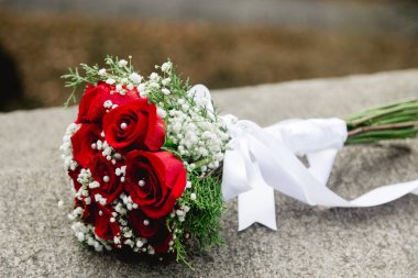 Çarpıcı bir buket kırmızı gül ve beyaz çiçek, gün ışığında doğa tarafından çevrelenmiş, taştan bir çıkıntının üzerinde yatıyor..