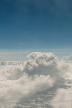 Pofuduk beyaz bulutlar parlak mavi bir gökyüzünde katmanlanır. Gün ortası uçuşu sırasında çarpıcı bir hava manzarası yaratır..