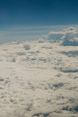 Bulutlar aşağıdaki araziyi kaplıyor. Yolculuk sırasında açık mavi gökyüzüne karşı yumuşak ve yumuşak bir arazi oluşturuyor..