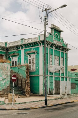 Yıpranmış bir turkuaz bina sessiz bir caddede bakımsız duruyor, klasik tarzını gösteriyor ve boyasını soyuyor..