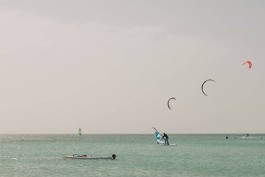 Rüzgâr sörfçüleri ve uçurtma sörfçüleri öğleden sonra bulutlu bir gökyüzünün altında suda faaliyetlerine devam ederler..