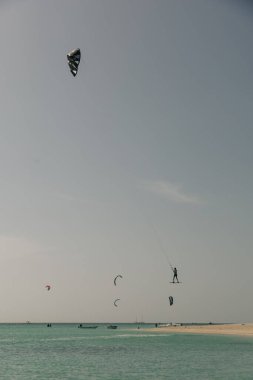 Uçurtmacılar güneşli bir günde, sakin turkuaz suların üzerinde havadan manevra yaparlar..