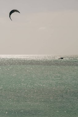 Bir uçurtma sörfçüsü parlak bir gökyüzünün altında süzülerek su sporlarının heyecanını gözler önüne serer..