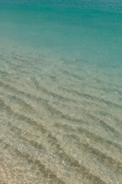 Sakin dalgalar güneşli bir günde sakin bir kumsalın yakınındaki berrak sularda dalgalanmalar yaratır..
