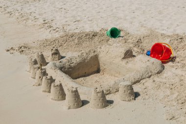 Çocuklar canlı bir plaja kumdan kale inşa ediyorlar. Etrafı kovalarla çevrili. Yaz eğlencesi ve yaratıcılığı sergiliyorlar..