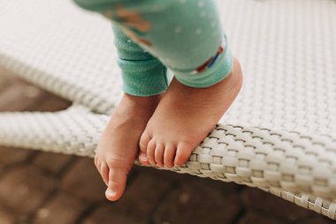 Genç bir çocuğun ayakları, güneşli bir ortamda denge ve neşe gösteren dokuma bir yüzeyin kenarına dokunur..