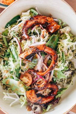 Renkli ızgara tavuk salatasında taze yeşiller, domatesler ve balkabağı tohumları sunuluyor ve sağlıklı bir yemek seçeneği sunuluyor..