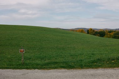 Kırsal alanda geniş yeşil bir yamaçta güneş uzaklardan batarken bir uyarı işareti vardır..