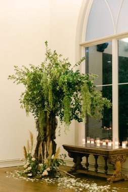 Yeşillik ve narin çiçekler ahşap bir masayı süslüyor. Yumuşak mum ışığında huzurlu bir atmosfer yaratıyor..