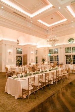 Zarif masalar, hafif ışıklandırma ve zevkli dekorların yer aldığı resmi bir etkinlik için hazırlanmış geniş bir ziyafet salonu..