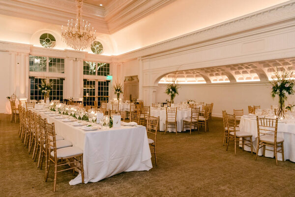 Столы, украшенные белыми скатертями и зеленью, накрыты для элегантного банкета в теплом помещении для мероприятий.