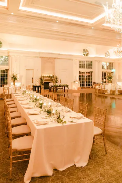 Zarif dekorasyonları olan uzun dikdörtgen masa bir etkinlik sırasında güzel aydınlatılmış bir ziyafet salonunda akşam yemeği için hazır..