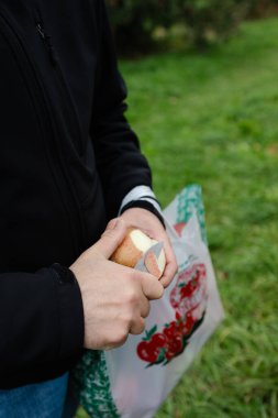 Bireyler, sonbaharda ağaçlarla çevrili taze çimlerin üzerinde dururken elmayı soymak için bıçak kullanırlar..