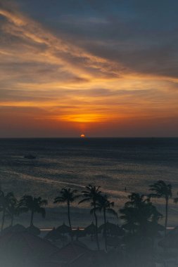 Altın güneş ufukta yavaşça batar, gökyüzünde sıcak renkler bırakır ve okyanus dalgalarını yansıtır..
