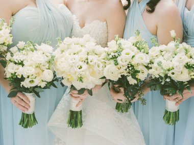 Zarif açık mavi elbiseli dört nedime açık hava düğününde çarpıcı beyaz çiçek buketleri tutuyor..