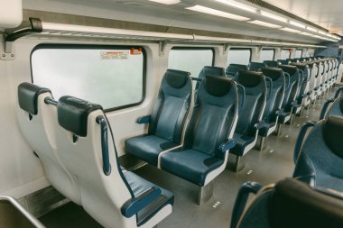 Temiz bir trenin içinde mavi ve beyaz koltuklar bulunur ve öğleden sonra banliyö boyunca sakin atmosferi vurgular..