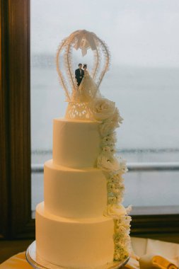 Beyaz katlı ve çiçekli muhteşem bir düğün pastası güzel bir arka planda durur..