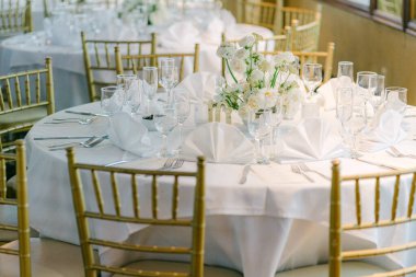 Yuvarlak masa beyaz çarşaflar ve çiçeklerle süslenmiş, resmi bir toplantı için bir ziyafet salonunda hazırlanıyor..
