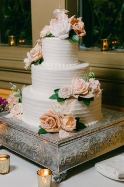 Üç katlı güzel bir düğün pastası pembe çiçeklerle zarif bir şekilde resepsiyon masasını süslüyor..