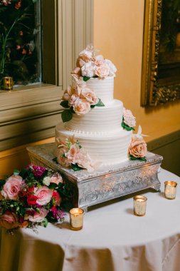 Üç katlı bir düğün pastası, sıcak mum ışığıyla çevrili bir masada pembe çiçeklerle güzelce süslenir..