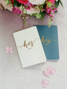 Arka planda pembe çiçekler olan bir masada dinlenen güzel yeminli kitapçıklar, düğün töreni için mükemmel..