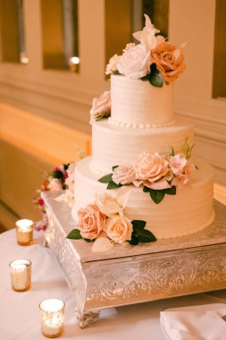 Taze güllerle süslenmiş, çok katlı göz kamaştırıcı bir düğün pastası güzel bir akşam yemeğinde sergileniyor..