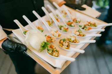 Garson, resmi bir toplantıda şık kaşıklarla servis edilen gurme aperatifleri sunar..