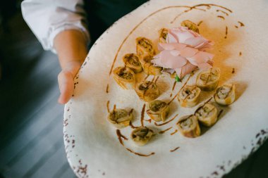 Bir insan, içinde hamur işleri ve zarif bir ortamda pembe bir çiçek süsü olan güzel bir tabak servis eder..
