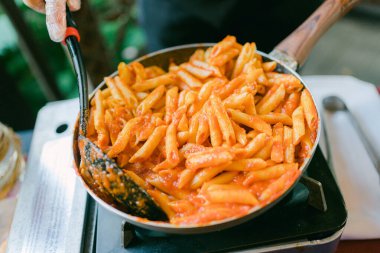 Şef domates soslu makarna pişiriyor açık hava yemek etkinliğinde portatif bir sobanın üzerinde..
