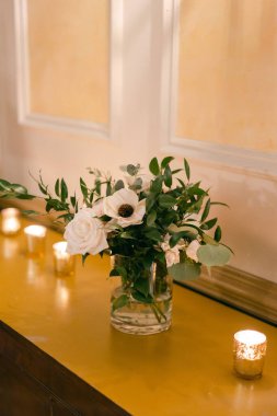 Yumuşak mum ışığıyla aydınlatılmış bir masanın üzerine yerleştirilmiş büyüleyici beyaz çiçekler ve yeşillik gösterisi..