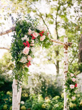 Bir yaz düğünü için açık havada pembe güller ve yemyeşil çiçeklerle süslenmiş bir çiçek kemeri..