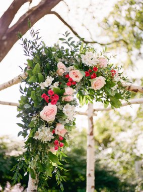 Yeşilliğin yanında pembe ve beyaz güllerden oluşan çarpıcı bir düzenleme güneşli bir parkta törensel bir kemeri süslüyor..