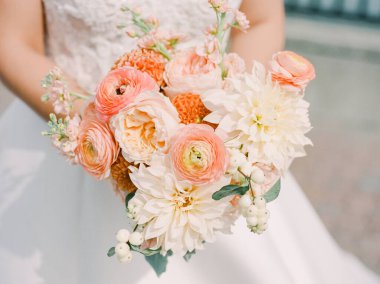 Bir gelin, özel gününde zarafet ve romantizm sergileyen şeftali ve beyaz çiçeklerden oluşan nefes kesici bir buket tutar..