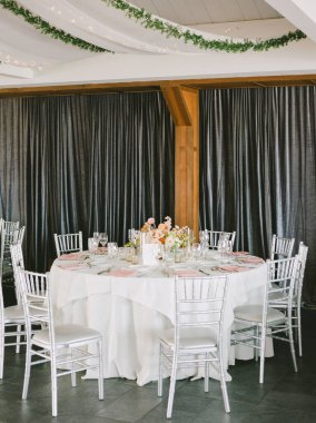 Yuvarlak masa, beyaz bir masa örtüsü, zarif yemek takımı ve çağdaş bir ortamda çiçek düzenlemeleri..