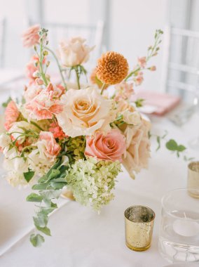 Güllerin ve mevsimlik çiçeklerin yer aldığı zarif buket, kutlama için hazırlanan bir düğün resepsiyonunda masayı süslüyor..