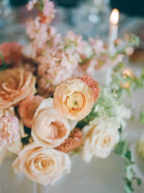 Güzel bir buket yumuşak renkli gül ve kır çiçekleri mum ışığında özel bir yemek masasını vurguluyor..