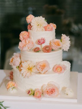 Üç katlı, pastel çiçeklerle süslenmiş, neşeli bir kutlama için huzurlu bir yere kurulmuş çarpıcı bir düğün pastası..