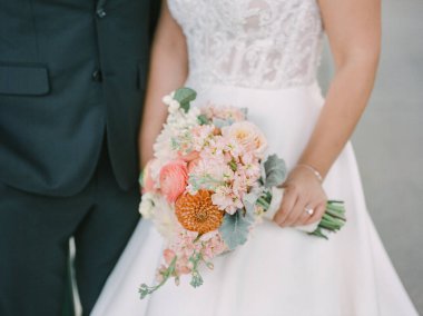 Gelin, ortağının yanında güneşli bir ortamda canlı bir çiçek buketi tutuyor..