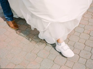 Beyaz gelinlik giymiş bir gelin, damadı ile yürürken spor ayakkabı giyer..