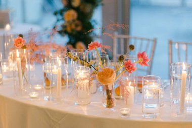 Dekoratif masa çiçekli cam vazolar, yumuşak mum ışığı ve akşam kutlaması için sıcak bir atmosfer içerir..