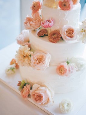 Çok güzel hazırlanmış düğün pastası yumuşak pastel çiçeklere sahiptir. Parlak bir ortamda romantik bir kutlama için mükemmeldir..