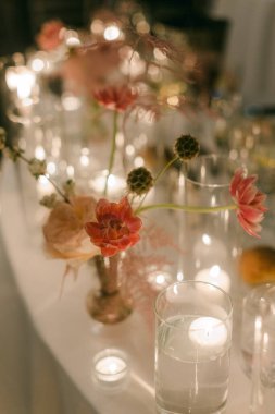 Çiçekler ve mumlar bir masayı süsler ve akşam vakti için sıcak bir ortam yaratır..