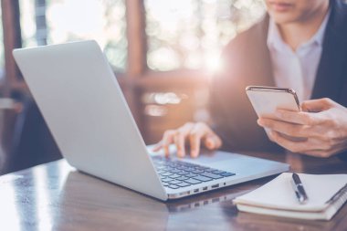 İş kadını cep telefonu kullanıyor, ofisteki dizüstü bilgisayarda çalışıyor, akıllı telefon kullanarak bilgiyi arıyor, ofis masasında dizüstü bilgisayarla internette geziniyor..