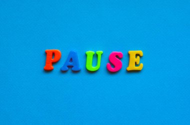 text pause from plastic colored letters on blue paper background