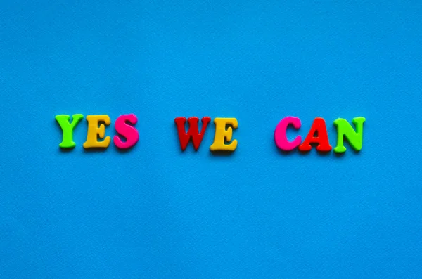 text yes we can from plastic colored letters on blue paper background