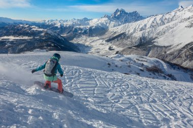 Bir kız, Tetnuldi, Mestia, Svaneti, Kafkasya 'daki Ushba zirvesinin arka planında snowboard' a biniyor.